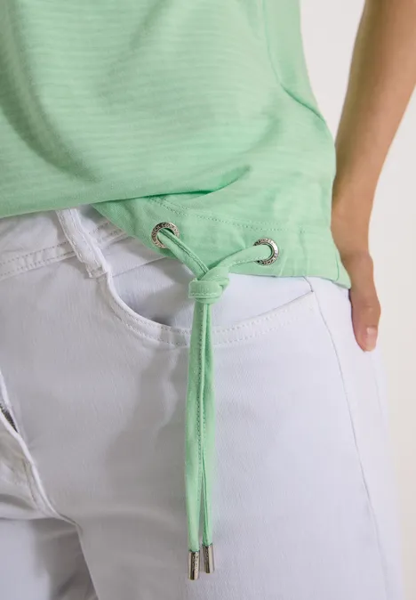 Haut vert clair noué à la taille, porté avec un jean blanc