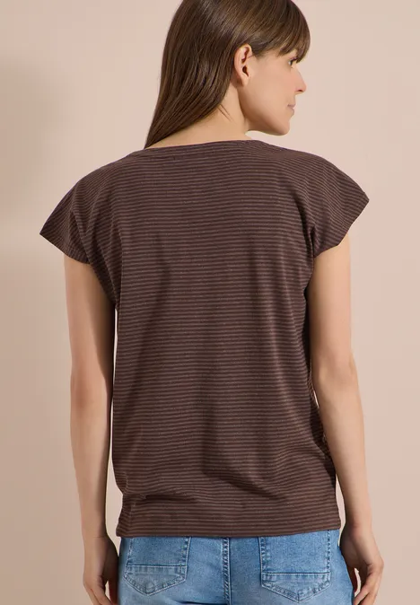 Rückansicht einer Frau in braun-schwarz gestreiftem T-Shirt und blauer Jeans vor beige-grauem Hintergrund