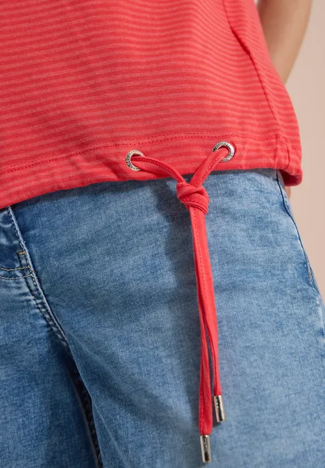 T-shirt rouge à rayures avec cordon noué à l’ourlet sur jean bleu.