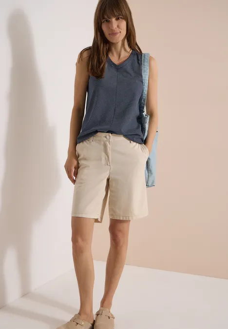 Top met V-hals en strepen universal blue Vrouw met mouwloos denim topje, beige korte broek, sneakers en lichtblauwe schoudertas voor een neutrale achtergrond.