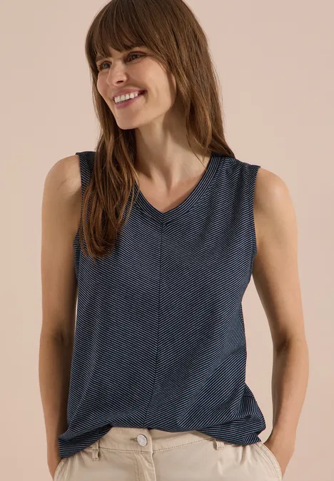 Top met V-hals en strepen universal blue Vrouw draagt donkerblauw mouwloos shirt met V-hals, handen in de zakken, voor een beige achtergrond.
