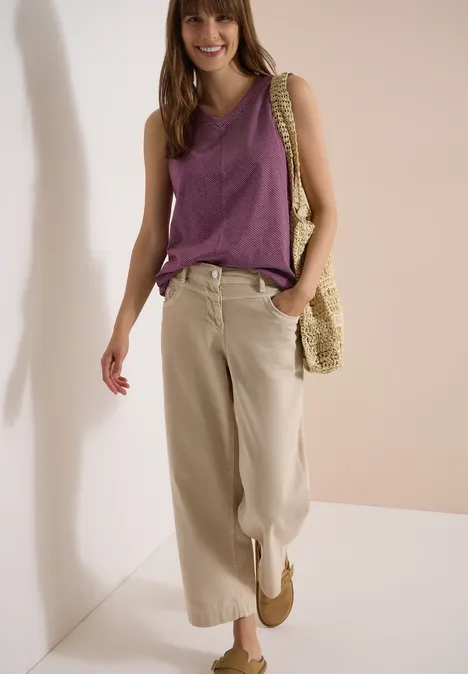 Top met V-hals en strepen sweet grape red Vrouw draagt paars mouwloos topje, wijde beige broek en strooien tas in een eenvoudige, lichte setting.