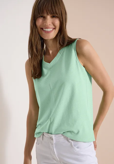 Top met V-hals en strepen juicy lime Vrouw draagt mintgroene mouwloze top en witte broek tegen neutrale achtergrond.