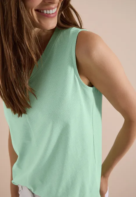 Top met V-hals en strepen juicy lime Een glimlachende vrouw in een mintgroene mouwloze top