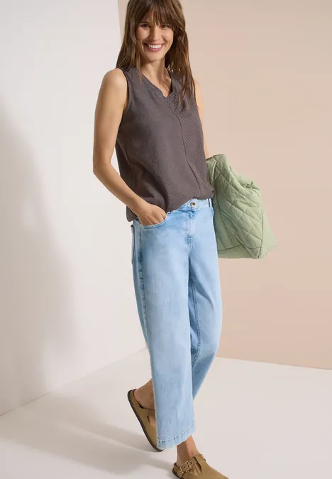 Frau in weitem Jeans und ärmellosem Top, trägt grüne Stepptasche.