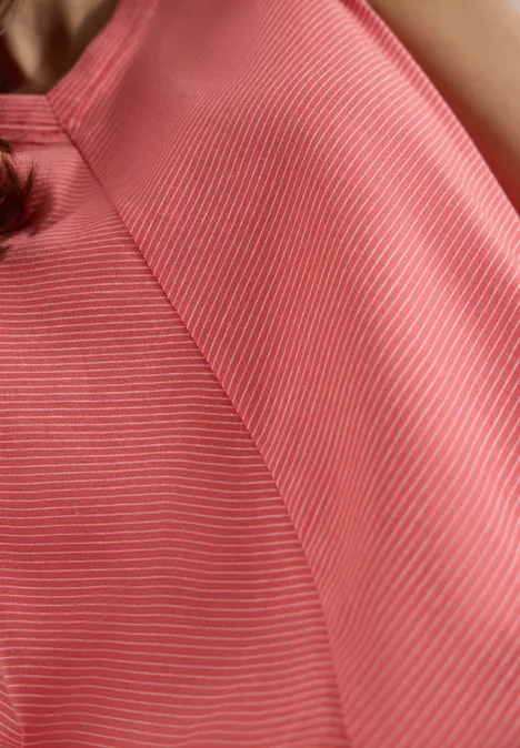 Top met V-hals en strepen coral Close-up van roze top met witte strepen op de schouder en borst van een persoon.