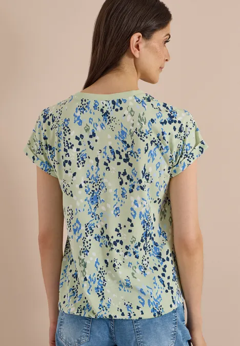 Frau von hinten in hellgrüner Bluse mit blauem Blumenmuster.