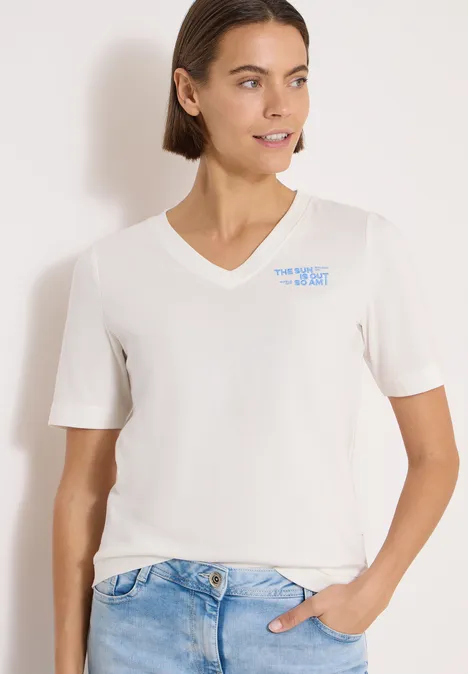Shirt met V-hals en tekstdetail vanilla white Vrouw draagt wit V-hals T-shirt en jeans, hand in de zak, voor een lichte achtergrond.