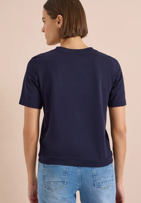Shirt met V-hals en tekstdetail urban dark blue Persoon van achteren met een donkerblauw t-shirt en een spijkerbroek.