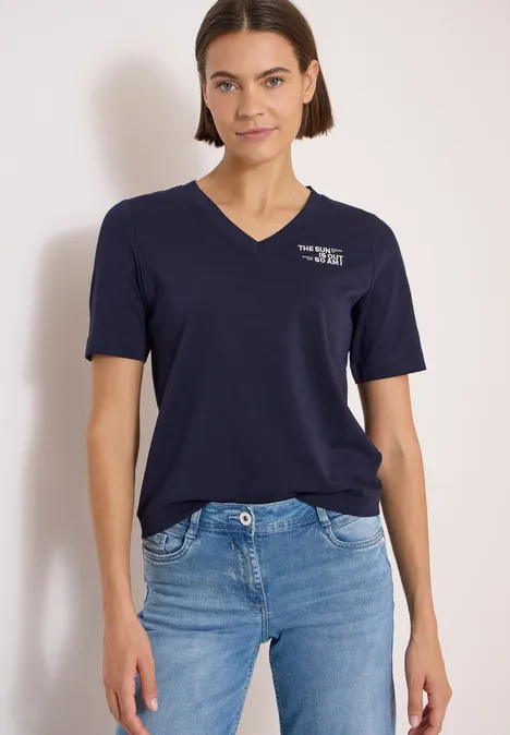Shirt met V-hals en tekstdetail urban dark blue Vrouw in wit T-shirt en blauwe spijkerbroek voor een lichte achtergrond.