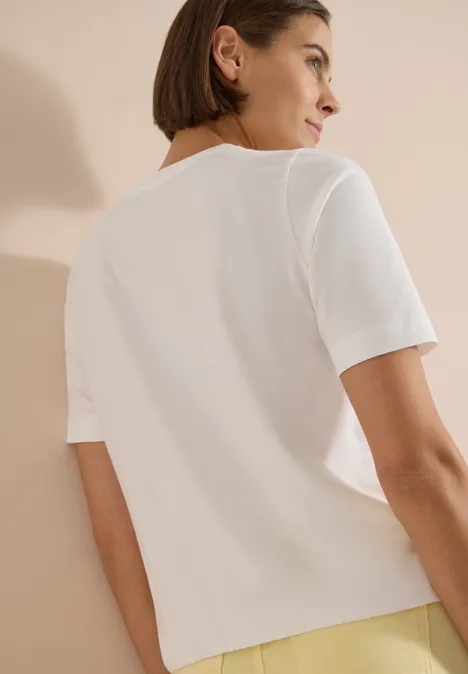 Vue de dos d'une personne portant un T-shirt blanc à manches courtes sur fond beige.