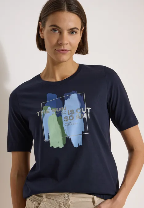 T-Shirt mit Rundhals und Frontprint urban dark blue Person trägt dunkelblaues T-Shirt mit abstrakten Pinselstrichen in Blau und Grün und Schriftzug.