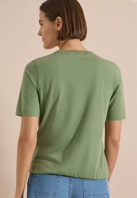 T-Shirt mit Rundhals und Frontprint deep matcha green Frau von hinten in schlichtem grünem T-Shirt, kurze braune Haare, neutraler Hintergrund.