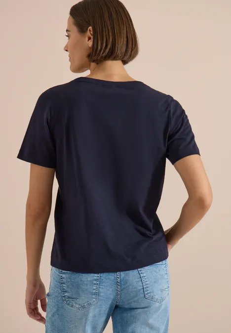 Shirt met ronde hals en opdruk aan de voorkant urban dark blue Persoon van achteren in een donkerblauw T-shirt en lichtblauwe spijkerbroek voor een beige achtergrond.