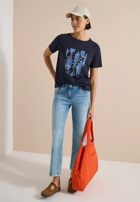 Shirt met ronde hals en opdruk aan de voorkant urban dark blue Vrouw in jeans, donkerblauw T-shirt met print, licht petje en grote rode tas.