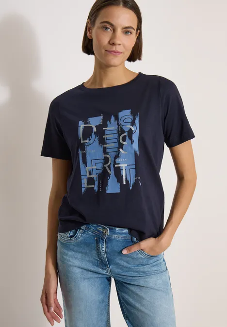 Shirt met ronde hals en opdruk aan de voorkant urban dark blue Vrouw draagt donkerblauw t-shirt met abstract lichtblauw motief en spijkerbroek, één hand in de zak.