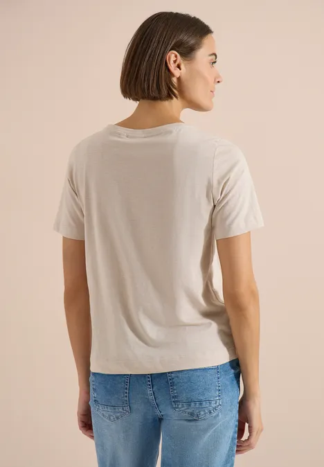 Een vrouw met kort bruin haar is van achteren te zien met een beige T-shirt en een blauwe spijkerbroek.