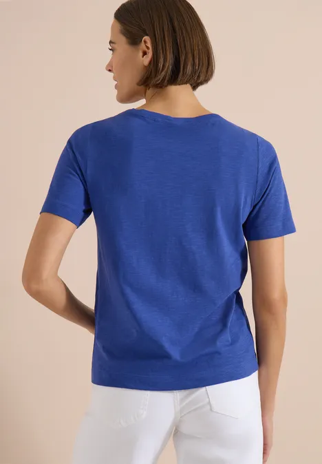 Achteraanzicht van een persoon in blauw shirt en witte broek.