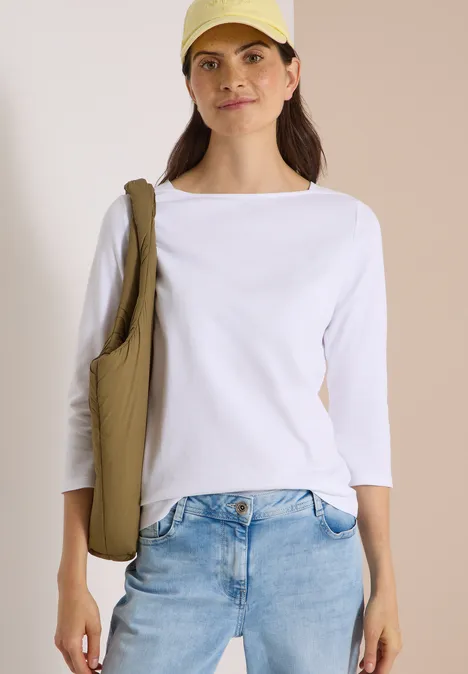 T-shirt basique à col bateau White Junge Frau in weißem 3/4-Arm-Shirt, Jeans und Cap trägt eine beige Umhängetasche.