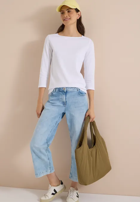 T-shirt basique à col bateau White Frau in weißem ¾-Arm-Shirt, hellblauen Jeans und gelber Cap trägt eine khakifarbene Tasche.