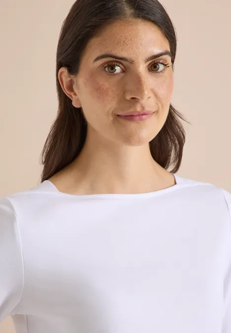 T-shirt basique à col bateau White Porträt einer jungen Frau mit dunklen Haaren in schlichtem weißen Oberteil vor neutralem Hintergrund.