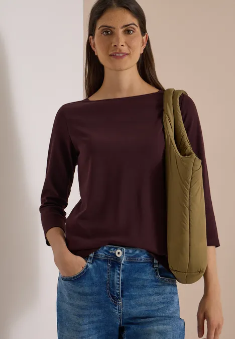 Basic Shirt met boothals berry red Frau trägt burgunderroten Pullover, Jeans und grüne Umhängetasche