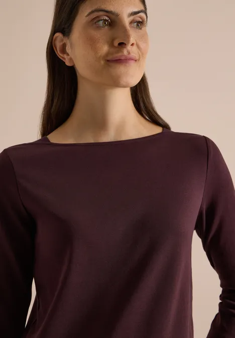 Basic Shirt met boothals berry red Porträt einer Frau im lila Langarmshirt, die seitlich in die Kamera blickt vor neutralem Hintergrund.