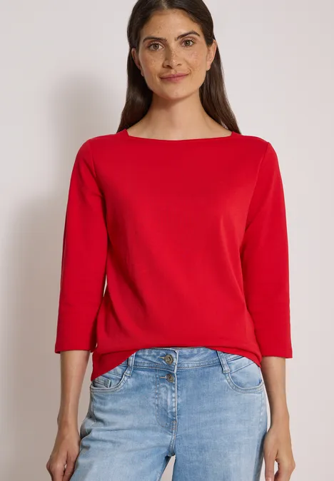 Basic shirt met boothals flame red Frau in rotem Dreiviertelärmel-Shirt und Jeans vor hellem Hintergrund