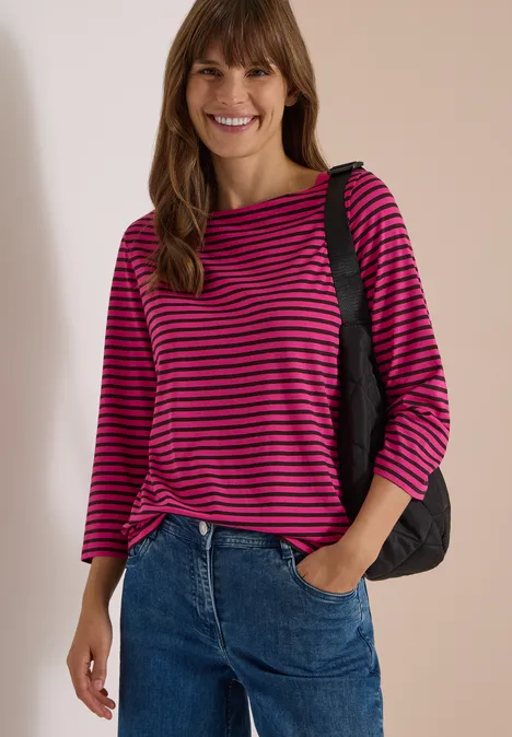 3/4-Arm Shirt mit Boat Neck und Streifen pink flash Eine lächelnde Frau trägt ein pink-schwarz gestreiftes Shirt, Jeans und eine schwarze Tasche über der Schulter.