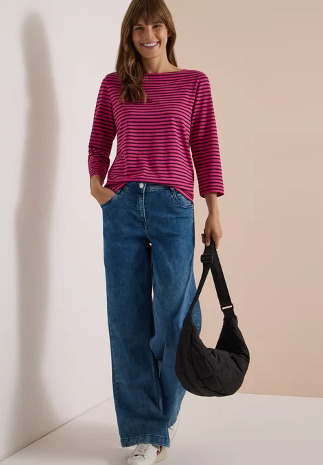 3/4-Arm Shirt mit Boat Neck und Streifen pink flash Frau in pink-gestreiftem Oberteil und weiter Jeans, trägt schwarze Tasche vor hellem Hintergrund.