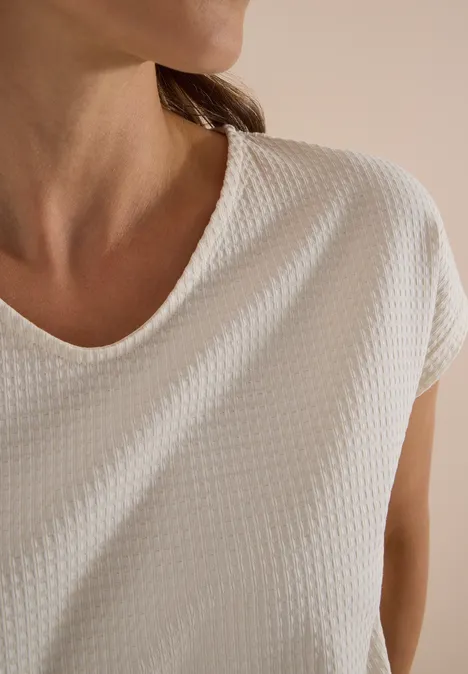 Oberkörper einer Person im strukturierten weißen T-Shirt, nur Hals und Schultern sichtbar.
