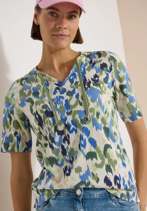 T-Shirt mit Split Neck und Print cashmere beige Person trägt kurzärmliges Oberteil mit abstraktem Blumenmuster in Grün, Blau und Weiß.