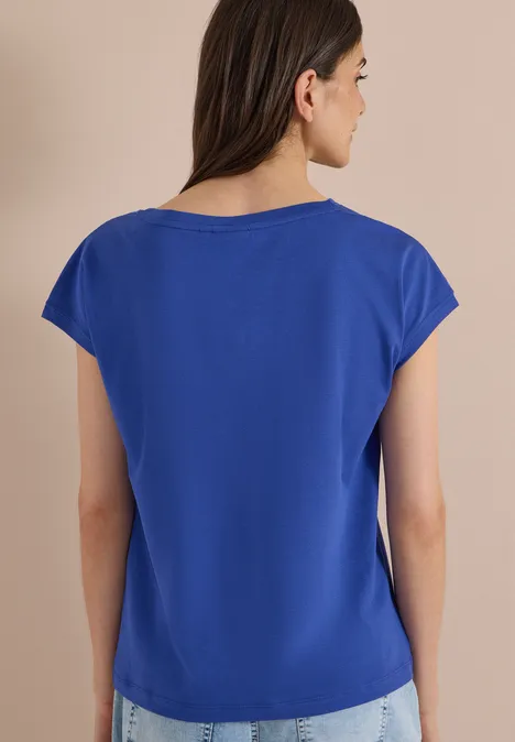 Rückansicht einer Person mit schulterlangem braunen Haar in schlichtem blauem T-Shirt.