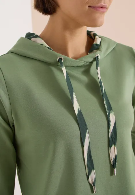 Grüner Hoodie mit gemusterten Kordeln in hellen Streifen, moderner Stil.