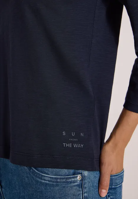 3/4-Arm Shirt in Unifarbe mit V-Neck urban dark blue Eine Person trägt ein dunkelblaues 3/4-ärmeliges Shirt mit Schriftzug "SUN THE WAY" und steckt die Hand in die Jeans.