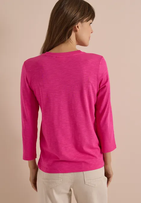 3/4-Arm Shirt in Unifarbe mit V-Neck pink flash Eine Frau von hinten in einem pinken 3/4-Arm-Shirt und beigen Hosen.