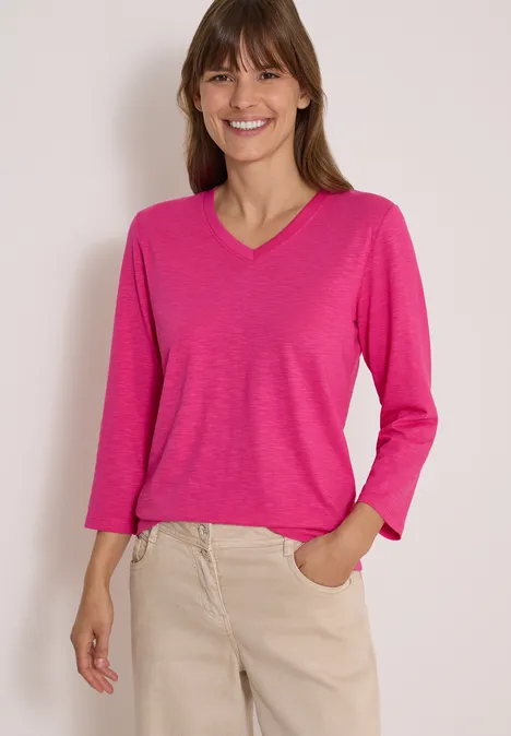 3/4-Arm Shirt in Unifarbe mit V-Neck pink flash Frau im pinken Langarmshirt mit V-Ausschnitt und beigen Hosen, lächelnd, Hand in Tasche.