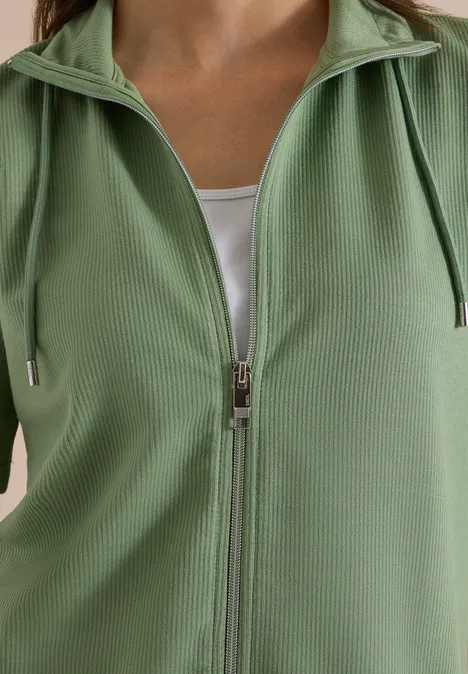 Nahaufnahme einer hellgrünen, gerippten Jacke mit Reißverschluss und weißem Top darunter.