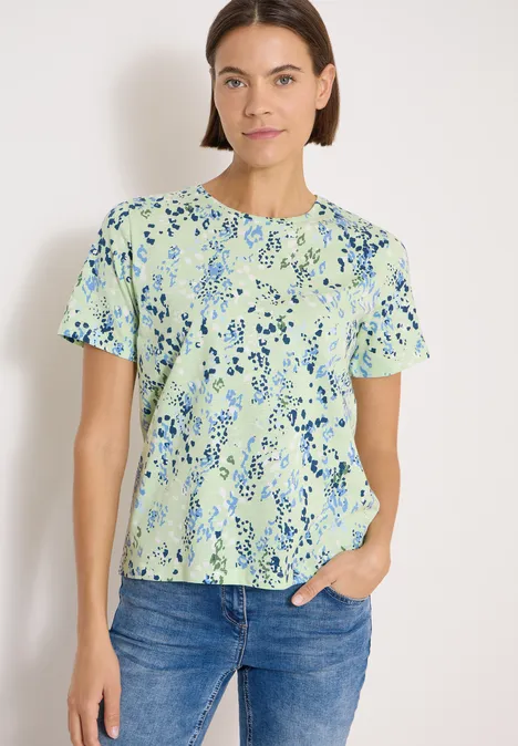 T-Shirt mit Rundhals und Print raw matcha lime Dame trägt grünes T-Shirt mit blauem Blumenmuster und Jeans vor hellem Hintergrund.