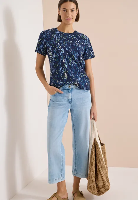 T-Shirt mit Rundhals und Print urban dark blue Frau in marineblauem Blumen-T-Shirt, hellen, weit geschnittenen Jeans und mit großer Korbtasche.