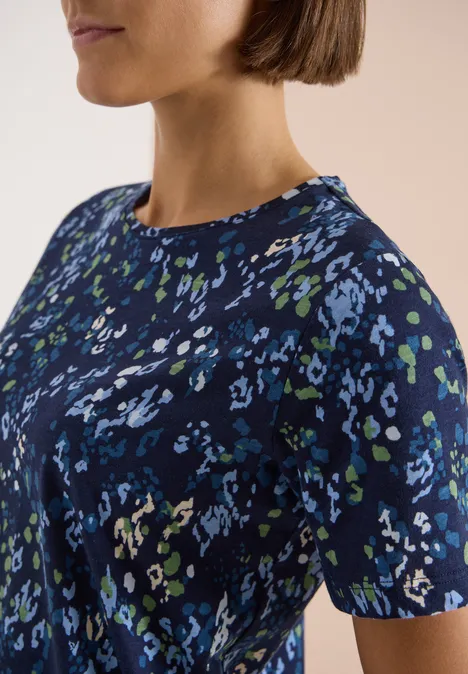 T-Shirt mit Rundhals und Print urban dark blue Nahaufnahme eines Oberkörpers in einem dunkelblauen Shirt mit abstraktem Fleckenmuster in Blau, Grün und Weiß.