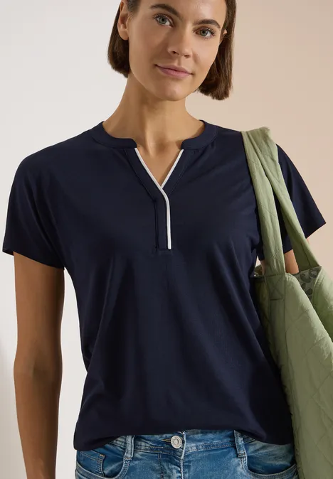 T-Shirt mit Split Neck in Unifarbe urban dark blue Frau in marineblauem T-Shirt mit kurzem Reißverschluss am Ausschnitt, trägt grüne Stofftasche.