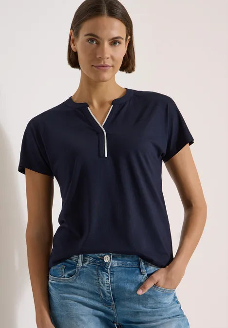 T-Shirt mit Split Neck in Unifarbe urban dark blue Frau in dunkelblauem Kurzarmshirt mit Knopfleiste und Jeans vor neutralem Hintergrund.