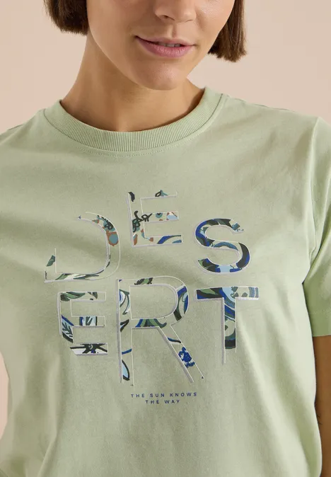 T-Shirt mit Rundhals und Frontprint raw matcha lime Frau trägt hellgrünes T-Shirt mit großem, floral gemustertem Schriftzug