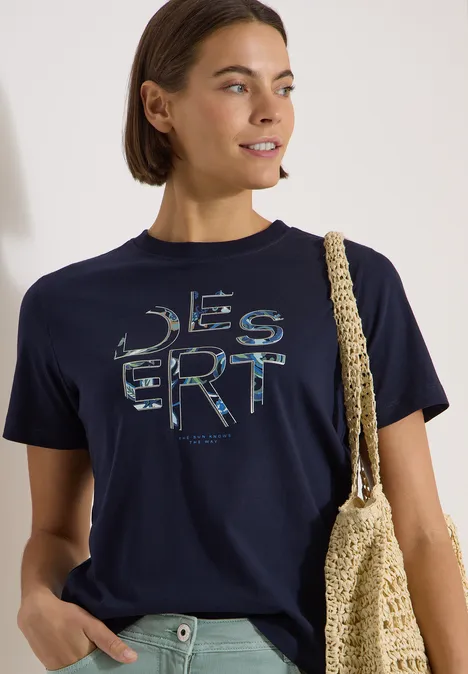 T-Shirt mit Rundhals und Frontprint urban dark blue Frau im dunkelblauen T-Shirt mit 'DESERT'-Schriftzug und gehäkelter Schultertasche.