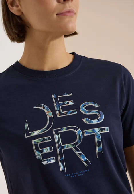 T-Shirt mit Rundhals und Frontprint urban dark blue Frau trägt ein dunkelblaues T-Shirt mit 'DESERT' in camouflageähnlichen Buchstaben.