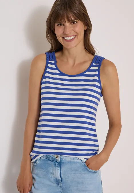 Femme souriante portant un débardeur rayé bleu et blanc, main dans la poche de son jean.