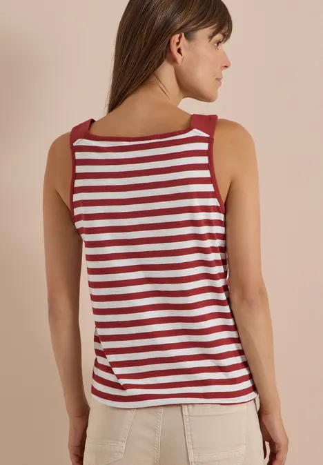 Femme de dos portant un débardeur rayé rouge et blanc et un pantalon clair, sur fond neutre.