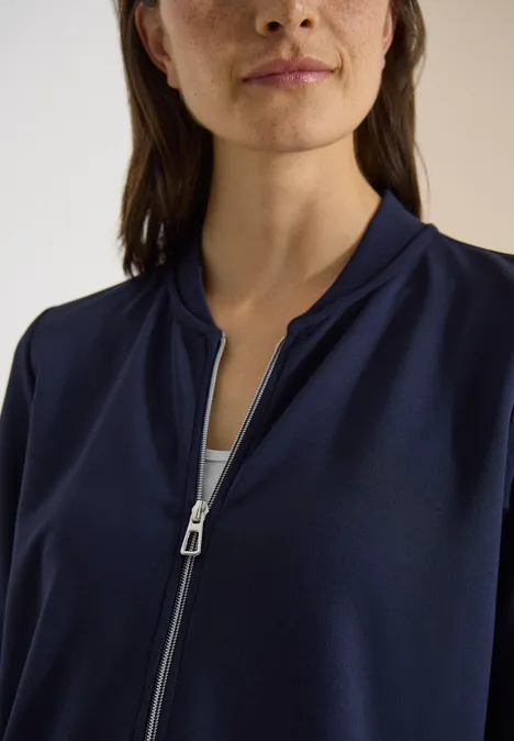 Frau trägt dunkelblaue Jacke mit offenem Reißverschluss, silberner Zipper sichtbar.