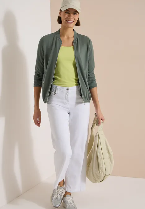 Langarm Jacke mit Rundhals und Zipper dried olive green Eine Frau trägt ein grünes Top, grüne Jacke, weiße Jeans und Sneakers, hält eine große Stofftasche.